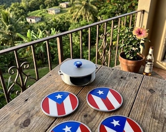 May include: A set of four circular coasters featuring the Puerto Rican flag design with red and white stripes and a blue triangle with a white star, accompanied by a matching round metal container with a blue knob on the lid.