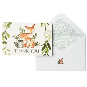 May include: A thank you card with a woodland theme. The card features a deer, a raccoon, a fox, and an owl surrounded by green leaves. The text "THANK YOU" is printed in black on the card.