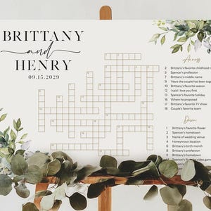 May include: A wedding crossword puzzle sign featuring the names "Brittany and Henry" and the date "09.15.2029". The sign includes a crossword grid with clues related to the couple, adorned with floral and greenery accents.
