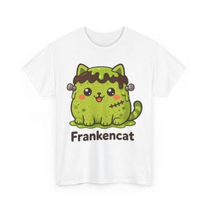 Op de afbeelding: Een wit t-shirt met een afbeelding van een groene kat met bruin haar, bouten op het hoofd en een gestikt litteken. De kat zit in een plas groen slijm en de tekst "Frankencat" is in donkerbruin onder de illustratie gedrukt.