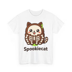 Op de afbeelding: Een wit t-shirt met een bruine cartoonkat met een schedelgezicht en botpatronen op het lichaam. De kat heeft een groen slijmaccent op het hoofd en de basis. Onder de kat staat de tekst Spookiecat in donkerbruine letters gedrukt.