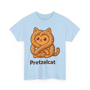 Op de afbeelding: Een lichtblauw t-shirt met een afbeelding van een bruine, met zout bestrooide krakeling in de vorm van een kat met oren en een staart. Onder de illustratie staat de tekst "Pretzelcat" in een donkerbruin, schreefloos lettertype.