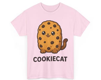 May include: A light pink short-sleeve t-shirt featuring a central graphic of a tan, oval-shaped cookie with dark brown chocolate chips, a cat-like face, paws, and a tail. The text COOKIECAT is printed in black capital letters below the graphic.