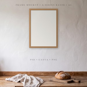 May include: A vertical light brown wooden picture frame mockup with a white centre, mounted on a textured white wall. Text above reads FRAME MOCKUP A-SERIES RATIO A4 and below reads PSD CANVA PNG. A wooden surface holds a loaf of bread and a cloth.