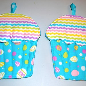 May include: Two blue and white cupcake-shaped pot holders with a pastel chevron pattern on the top and an Easter egg pattern on the bottom.