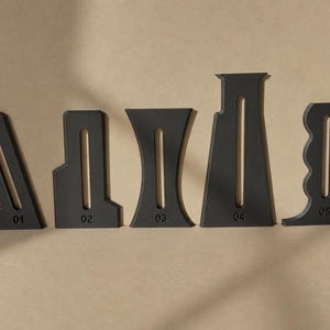 May include: A set of five matte black acrylic templates, each featuring a central vertical slot and a unique geometric silhouette. The pieces are numbered 01 through 05 at the base, showcasing distinct shapes including angled, stepped, curved, and wavy edges.