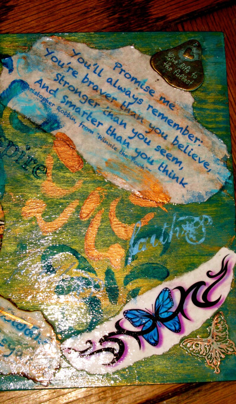 May include: A wooden box with a blue, green, and gold background. The box has a quote from Winnie the Pooh about being brave, strong, and smart. The box also has a butterfly and a metal charm with the words "Live life to the fullest".