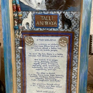 May include: A framed artwork with a blue and brown background. The artwork features a quote about two wolves, one representing good and the other representing evil. The quote is attributed to a Cherokee parable. The artwork also features a pair of wolves, one white and one black, with a beaded necklace.