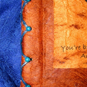 May include: A brown leather-bound journal with blue beads along the spine. The journal has a handwritten message on the front cover that reads "You're beautiful."