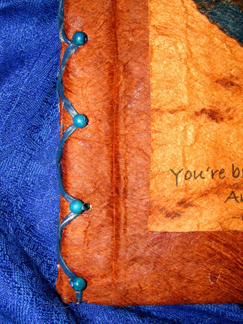May include: A brown leather-bound journal with blue beads along the spine. The journal has a handwritten message on the front cover that reads "You're beautiful."