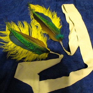 May include: Two yellow and green peacock feathers attached to a cream-colored fabric headband.