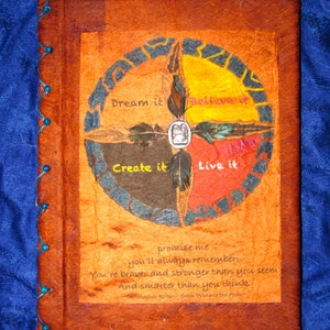 May include: A brown leather-bound journal with a colorful circular design on the front cover. The design features four sections with the words "Dream it", "Believe it", "Create it", and "Live it" written in white. The journal has a quote from Winnie the Pooh: "Promise me you'll always remember: You're braver and stronger than you seem and smarter than you think."