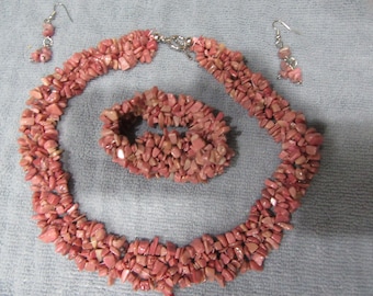 May include: A pink gemstone jewelry set with a necklace, bracelet, and earrings. The necklace and bracelet are made of small, irregular shaped pink stones. The earrings are simple silver hooks with a single pink stone.