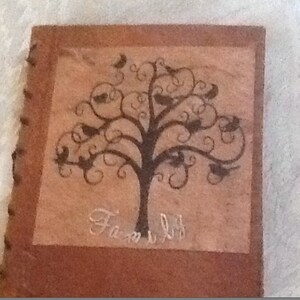 May include: A brown leather-bound photo album with a decorative tree design and the word "Family" written in white script. The tree has black branches and leaves with small birds perched on them.
