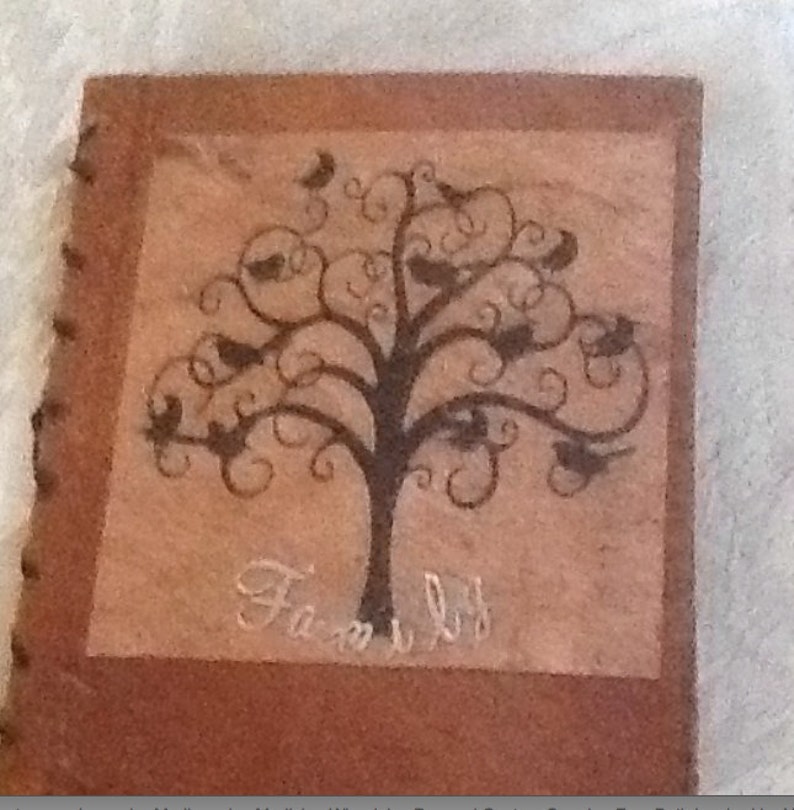 May include: A brown leather-bound photo album with a decorative tree design and the word "Family" written in white script. The tree has black branches and leaves with small birds perched on them.