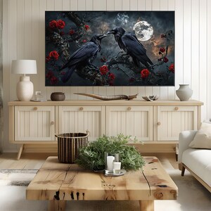 May include: A framed artwork depicts two black ravens perched on a branch with red roses, set against a night sky with a full moon. The artwork is displayed above a light wood cabinet with a natural wood coffee table in a living room setting.