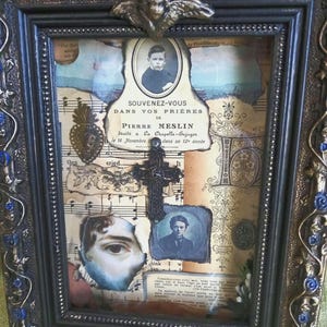 Könnte beinhalten: Verziertes gerahmtes Kunstwerk mit Vintage-Ästhetik. Der Rahmen ist dunkel mit goldenen und blauen Akzenten. Im Inneren befindet sich eine Collage mit Porträts, Notenblättern und Textfragmenten, darunter "SOUVENEZ-VOUS DANS VOS PRIÈRES DE PIERRE MESLIN". Ein kleines Kreuz ist ebenfalls enthalten.