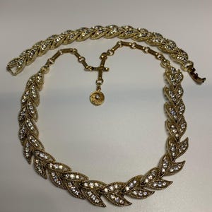 May include: A gold tone necklace with a leaf design and clear rhinestones. The necklace has a chain extender.