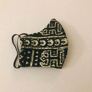 May include: Black and white face mask with a geometric pattern. The mask has a black elastic band.