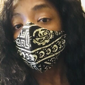 May include: A person wearing a black and white patterned face mask with geometric designs. The mask covers the nose and mouth.
