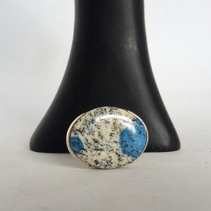 Könnte beinhalten: Ein runder, weißer und blauer Stein-Cabochon, der in einen silbernen Ring gefasst ist. Der Stein hat ein gesprenkeltes Muster mit blauen Akzenten.