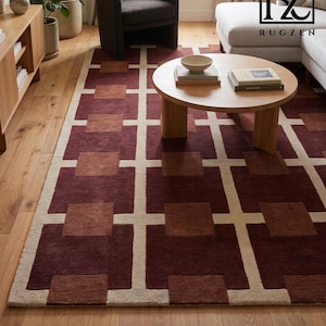 May include: A rectangular area rug featuring a geometric grid pattern in deep burgundy, muted terracotta, and cream. The design consists of large squares connected by intersecting lines, creating a structured, repeating motif across the surface.