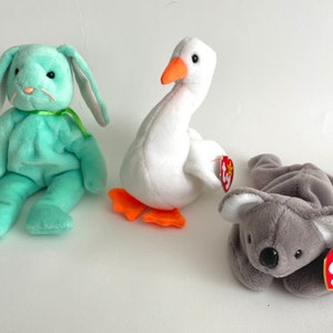 May include: Three plush toys: a light green bunny, a white goose with orange feet, and a gray koala. Each toy has a red heart-shaped tag with the word "Ty" and a star.