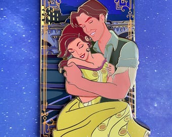 May include: A gold-framed enamel pin featuring a couple embracing. The woman is wearing a yellow dress and the man is wearing a green shirt. The background is a blue night sky with a cityscape.