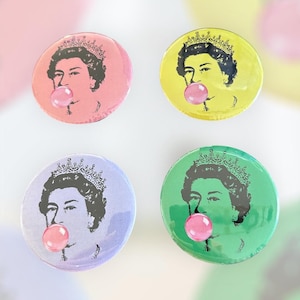 Peut inclure: Quatre badges ronds avec un design pop art. Chaque badge présente une illustration en noir et blanc d'une personne portant une couronne et soufflant une bulle de chewing-gum. Les badges sont roses, jaunes, violets et verts.