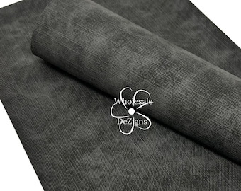 May include: A rectangular sheet of dark charcoal gray faux leather material with a subtle, distressed texture and a visible diagonal weave pattern. A white logo featuring a stylized flower and the text Wholesale DeZigns is printed on the surface.