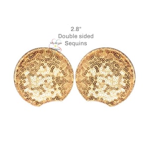 May include: Two circular ear-shaped accessories covered in shimmering gold sequins. The text 2.8" Double sided Sequins is printed above the items, along with a small logo for Wholesale DeZigns. The accessories feature a rounded top edge.