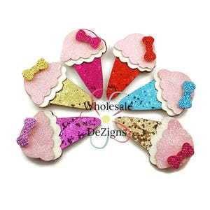 May include: A selection of glittery ice cream cone-shaped decorations in various colours. Each cone has a different colour, including pink, red, blue, gold, and purple, and is topped with a matching bow. The text "Wholesale DeZigns" is visible.