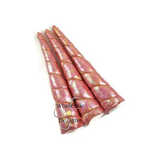 May include: Three pink unicorn horns with a metallic sheen and gold trim. The horns are spiraled and have a soft, plush appearance. The horns are arranged on a white background.
