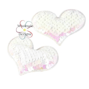 May include: Two heart-shaped patches covered in white and iridescent pink sequins. The sequins are arranged in rows, creating a shimmering texture. A logo with the text Wholesale DeZigns is visible near the top heart-shaped patch.