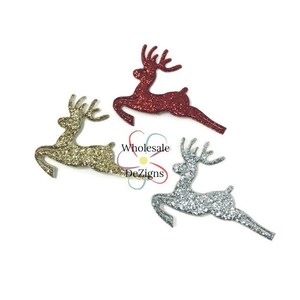May include: Glittery reindeer cutouts in gold, silver, and red. The reindeer are in a leaping pose, with detailed antlers. The image includes the text "Wholesale Dezigns". These festive decorations are perfect for holiday crafts and embellishments.