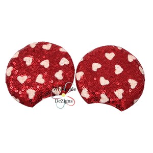 Peut inclure: Une paire d'accessoires de tête en forme d'oreilles circulaires recouverts de sequins rouges avec un motif répétitif de petits cœurs rose clair. Le texte Wholesale DeZigns est imprimé au centre entre les deux pièces en noir et rouge.