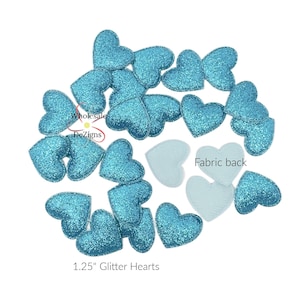 May include: A collection of 1.25-inch glitter hearts in various shapes and sizes. The hearts are a vibrant teal color and have a sparkling glitter finish. Some hearts have a fabric back. The image includes the text "Wholesale DeZigns".