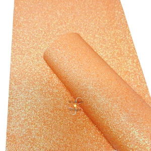 May include: A sheet of peach-colored glitter fabric with iridescent shimmer. The fabric is folded in half and the brand name "Wholesale DeZigns" is visible in the lower right corner.