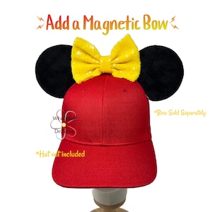 May include: A red baseball cap with black mouse ears and a yellow sequined bow. The text "Add a Magnetic Bow" is above the cap. The text "*Bow Sold Separately" and "*Hat not included" are also visible.