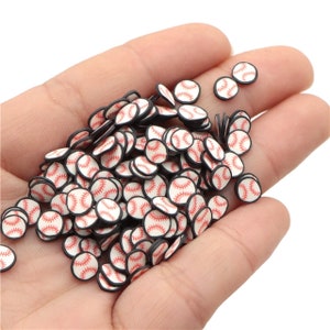 May include: A collection of small, baseball-themed polymer clay slices. Each slice features a white baseball design with red stitching and a black border. The slices are held in a hand, creating a visually appealing arrangement.
