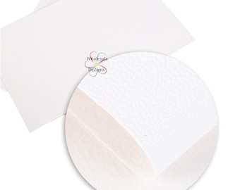 May include: A rectangular sheet of white faux leather material with a textured surface. A circular inset shows a magnified view of the grain pattern. The logo Wholesale DeZigns is printed in the centre with a colourful flower graphic icon.