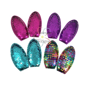May include: A selection of oval sequin appliques in vibrant colours: fuchsia, teal, purple, and a rainbow mix. Each applique is covered in shimmering sequins, ideal for adding sparkle to garments or accessories.