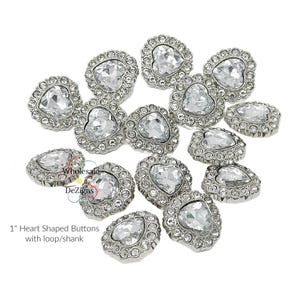 May include: A scattering of 1 inch heart-shaped buttons with a clear crystal centre and a silver metal rim. Each button has a loop shank.