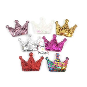 May include: Assortment of seven sparkly crown-shaped embellishments in various colors, including pink, gold, silver, white, red, and iridescent.