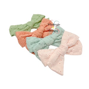 May include: Three handmade fabric hair bows in pastel colors. The bows are made of a soft, textured fabric with a delicate eyelet pattern. The colors are light green, peach, and light pink.