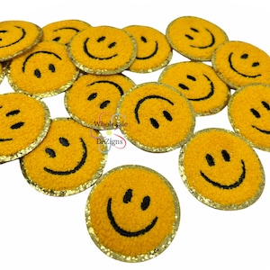 May include: A collection of circular yellow patches featuring a black embroidered smiley face design. Each patch has a textured surface and a shimmering gold border. The text Wholesale DeZigns is printed in the center of the image arrangement.