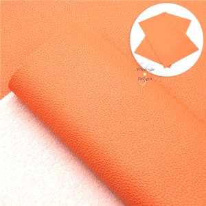 May include: A sheet of bright orange faux leather material with a distinct pebbled texture. The material is shown rolled in the foreground, while a circular inset in the upper right corner displays two flat, overlapping sheets of the same orange material.