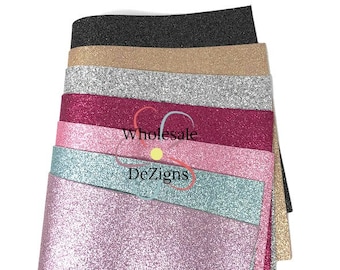 May include: A stack of glitter sheets in various colors, including black, gold, silver, and shades of pink and blue. The sheets have a sparkling texture and are arranged in a layered pattern. The text "Wholesale DeZigns" is visible.