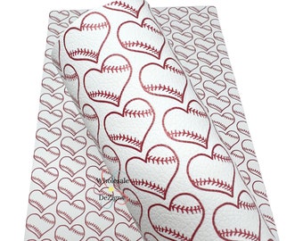 May include: A sheet of white faux leather material featuring a repeating pattern of red heart shapes. Each heart is designed with the texture and stitching details of a baseball. The surface has a visible grain, and the text Wholesale DeZigns is printed in the centre.