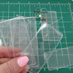 May include: A stack of clear plastic sleeves for protecting cards or other small items. The sleeves are on a green cutting mat with a ruler.